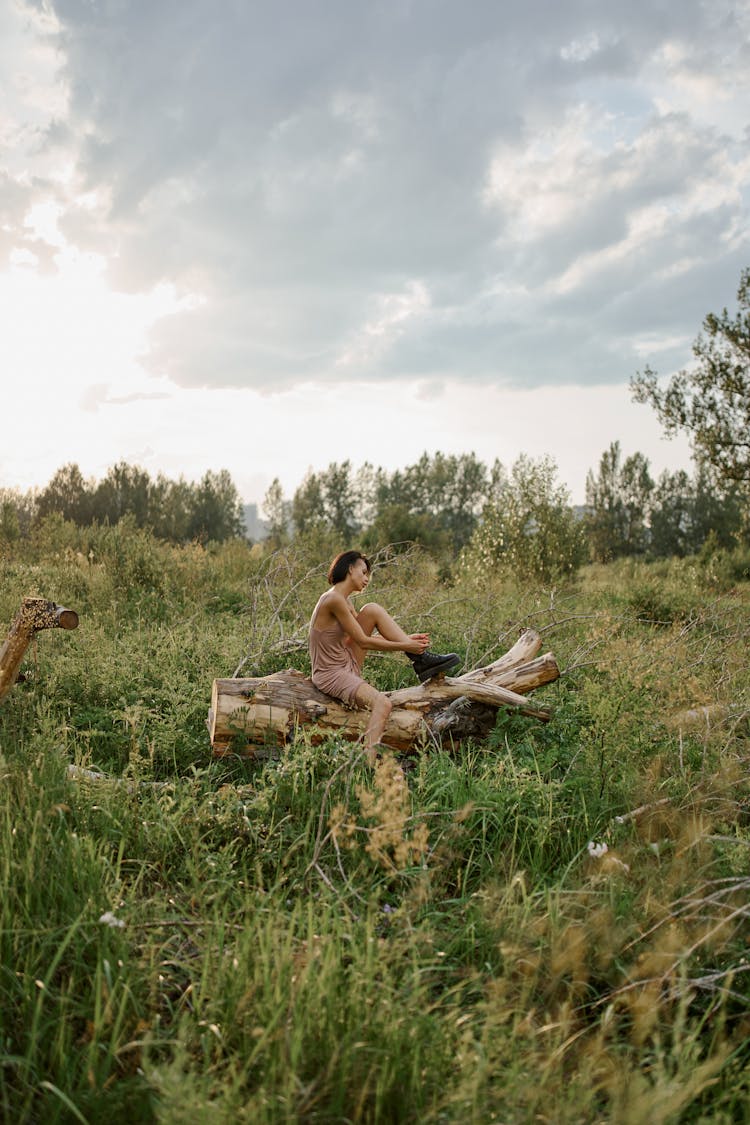 Anonymous Woman Putting On Footwear On Tree Trunk In Countryside