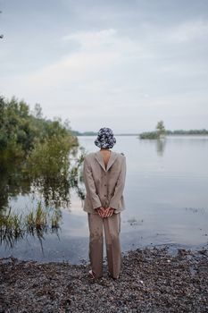 在多云的天空下，一位时尚女士双手背在身后，欣赏着河流的背影