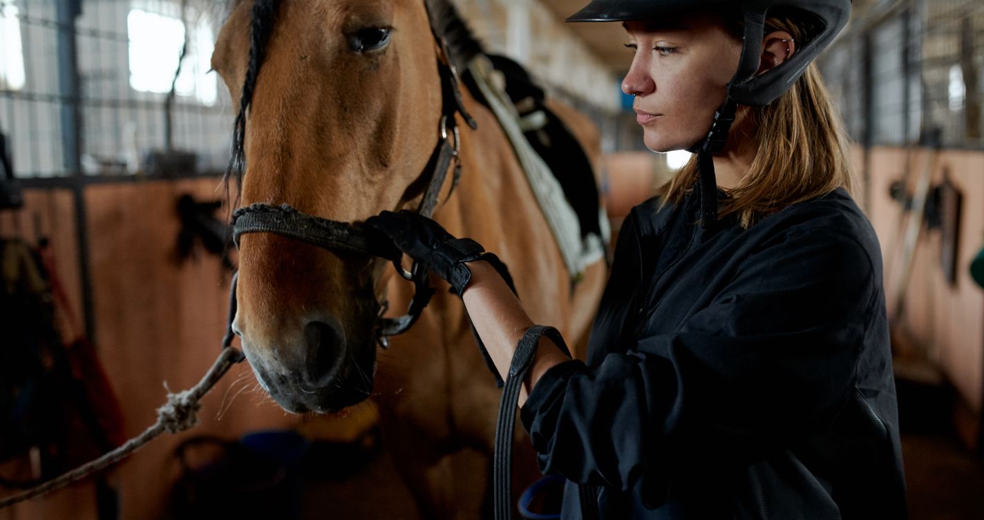 Femme portant une bombe de protection équestre auprès d'un cheval dans une écurie