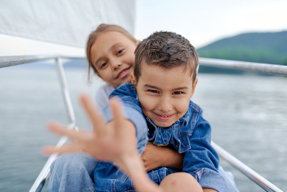 Smiling little girl hugging playful brother while having fun on yacht in sea and looking at camera