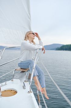 一位穿着休闲装的年轻女子在帆船上放松身心，享受着夏日平静的海景