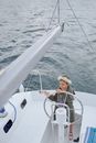 High angle of child in flower wreath and summer clothes standing near helm while floating on yacht