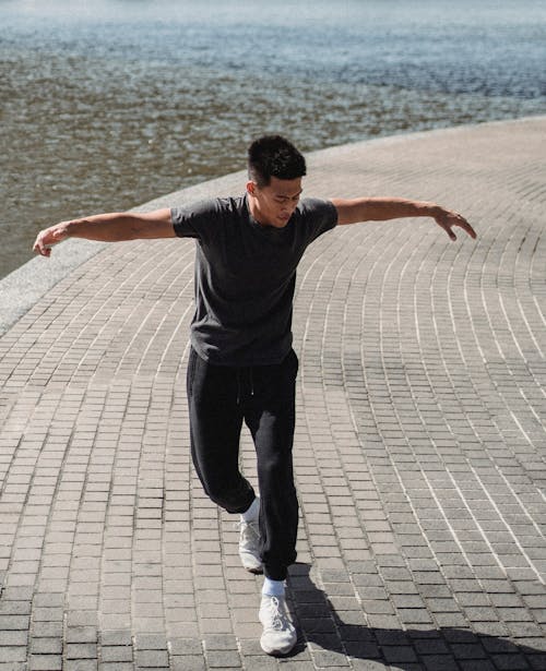 Asian break dancer with raised arms on embankment