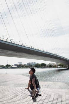 A young man performs a yoga twist pose outdoors by an urban bridge, embodying health and serenity.