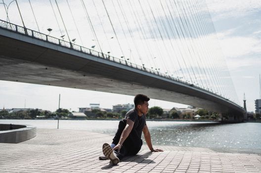一名年轻的少数族裔男子在河流和桥梁附近练习瑜伽，目光却移向别处
