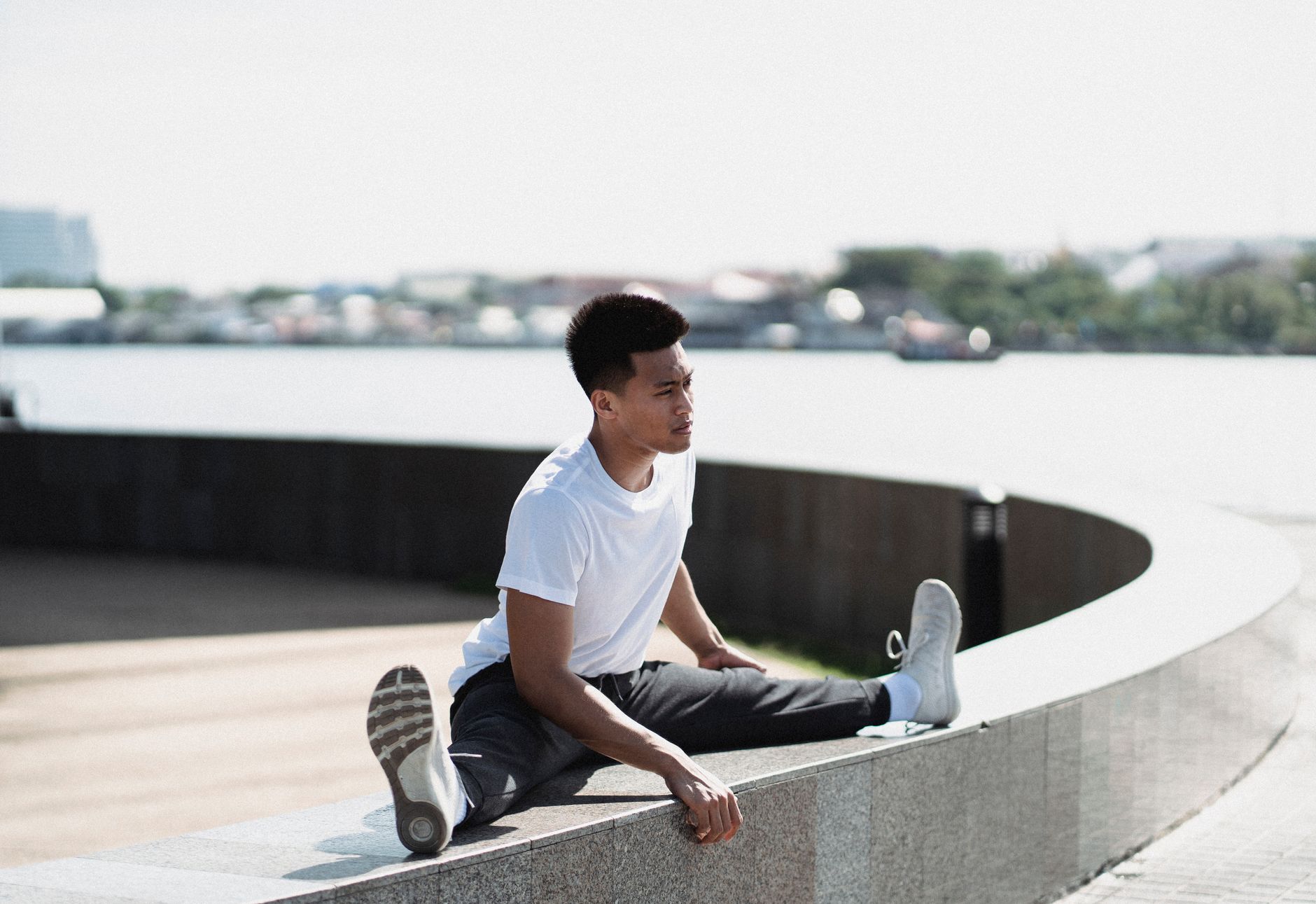 Flexible Asian sportsman sitting on border and stretching legs