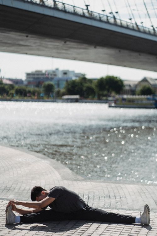 Free Full body unrecognizable flexible male wearing sports clothes doing split and stretching body while exercising on paved city promenade on sunny warm day Stock Photo