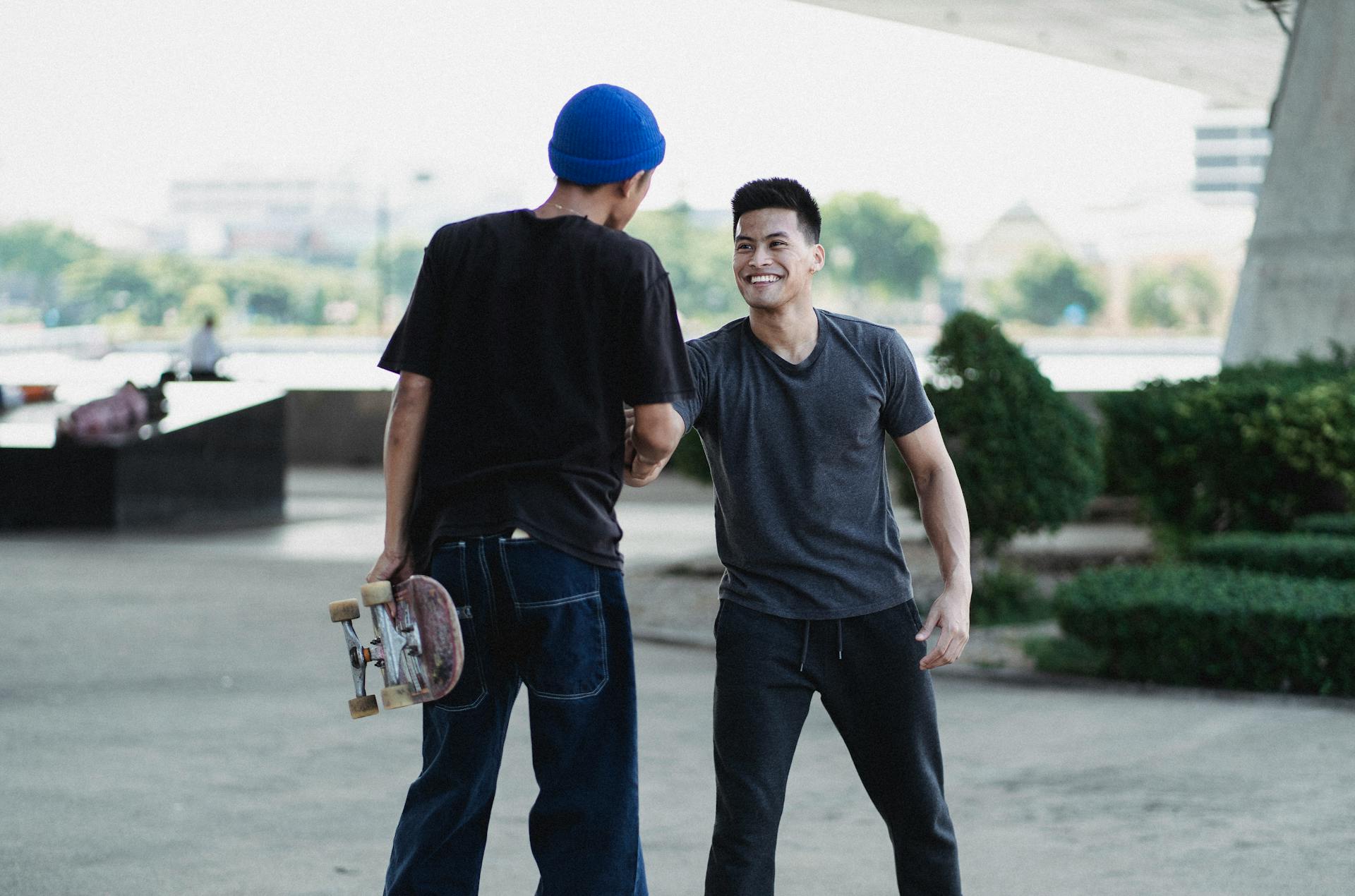 Smiling Asian men in street style clothes shaking hands and greeting each other while standing on sunny street