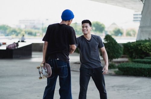 Free Smiling Asian men in street style clothes shaking hands and greeting each other while standing on sunny street Stock Photo
