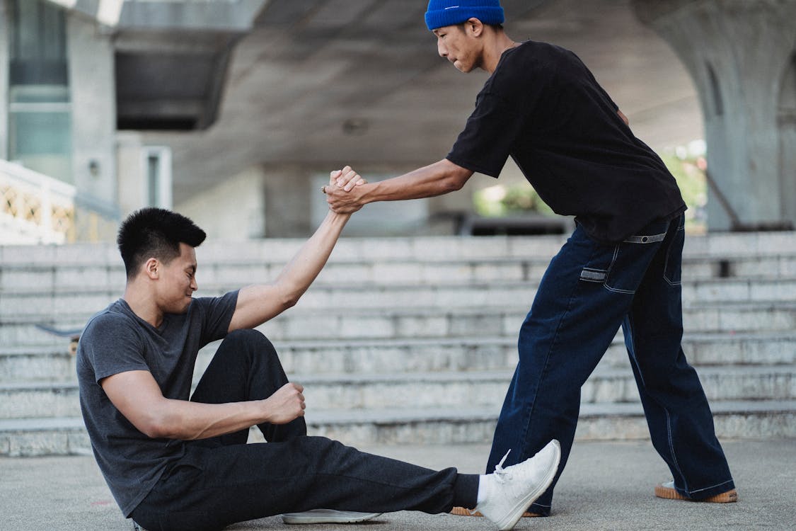 Free Asian man helping friend to get up from ground Stock Photo