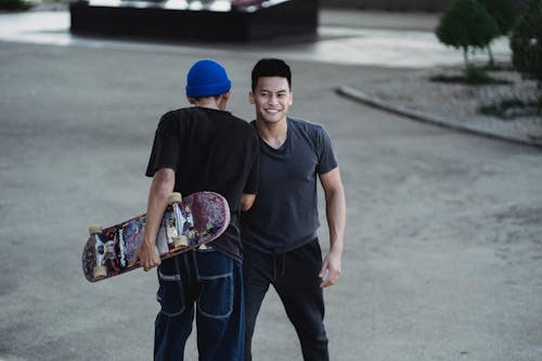 Free Cheerful young Asian men in casual clothes bumping shoulders and smiling while greeting each other on street Stock Photo