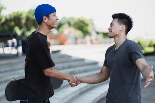 美滿的亞洲男子在陽光明媚的大街上握手