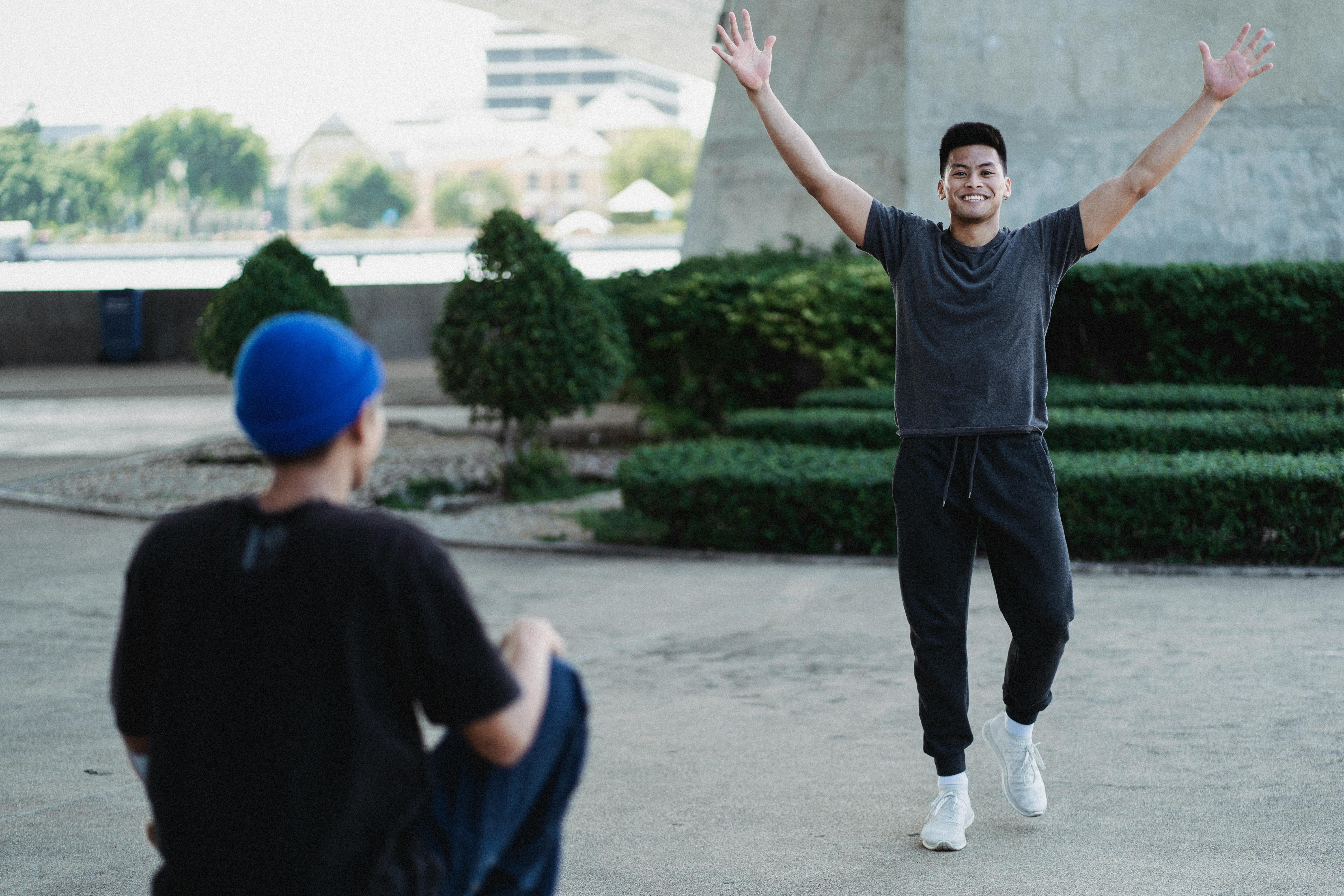 cheerful asian man raising arms in excitement on sunny street