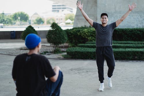 Happy smiling Asian man raising arms in satisfaction while spending sunny day outside with friend and looking at camera