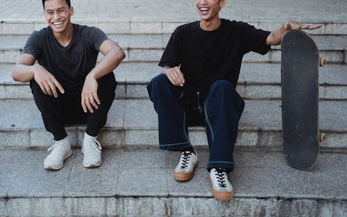 Free Crop cheerful Asian male friends resting on street steps Stock Photo
