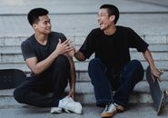 Laughing Asian male skaters resting on street staircase