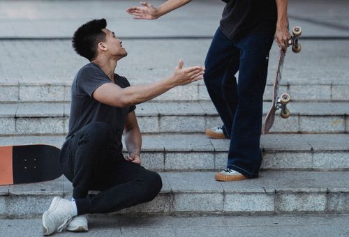 Free Smiling Asian male friends with skateboards clapping each others hands while greeting or saying goodbye on stone street staircase Stock Photo