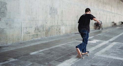 Full body of faceless teenage skater in casual outfit practicing skateboard riding on paved street