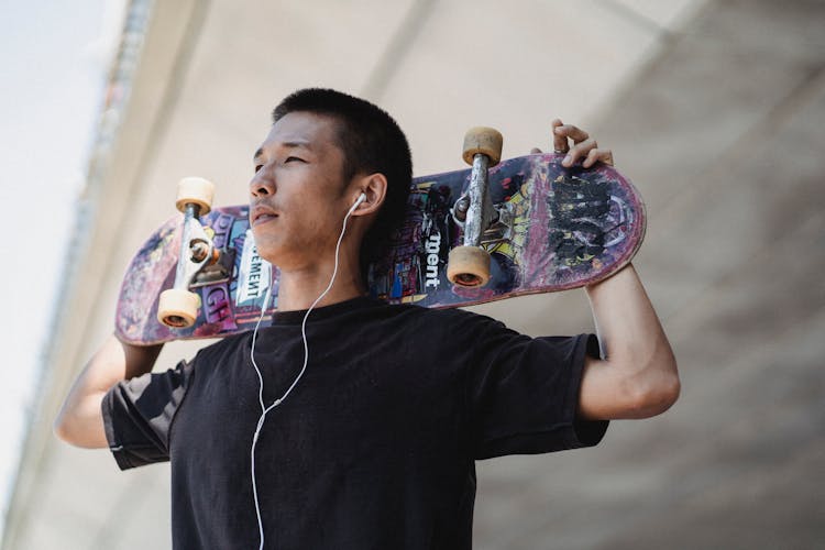 Asian Man With Skateboard On Street