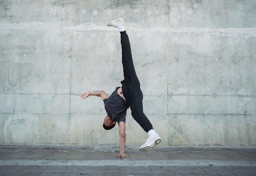 Flexible male dancer in sportswear and white sneakers doing handstand during break dance on urban street