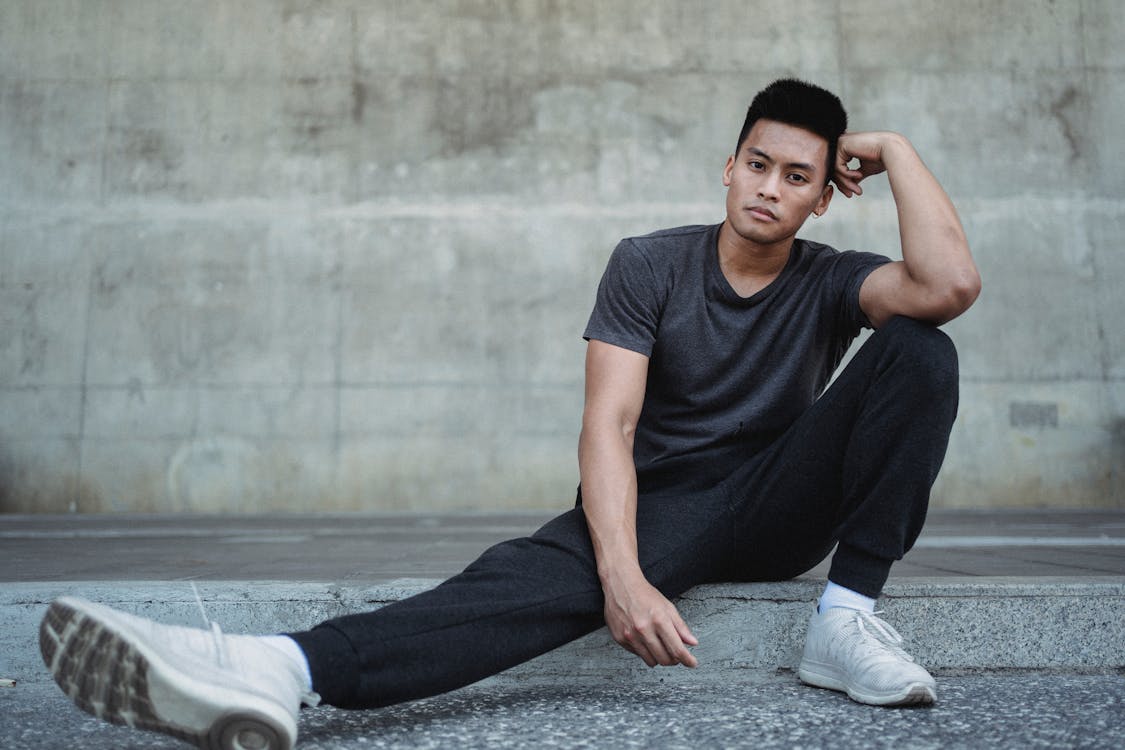 Young Asian man sitting on sidewalk and leaning hand on leg · Free ...