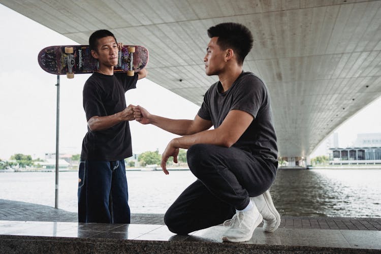 Young Friends Giving Fist Bump On Promenade Under City Bridge