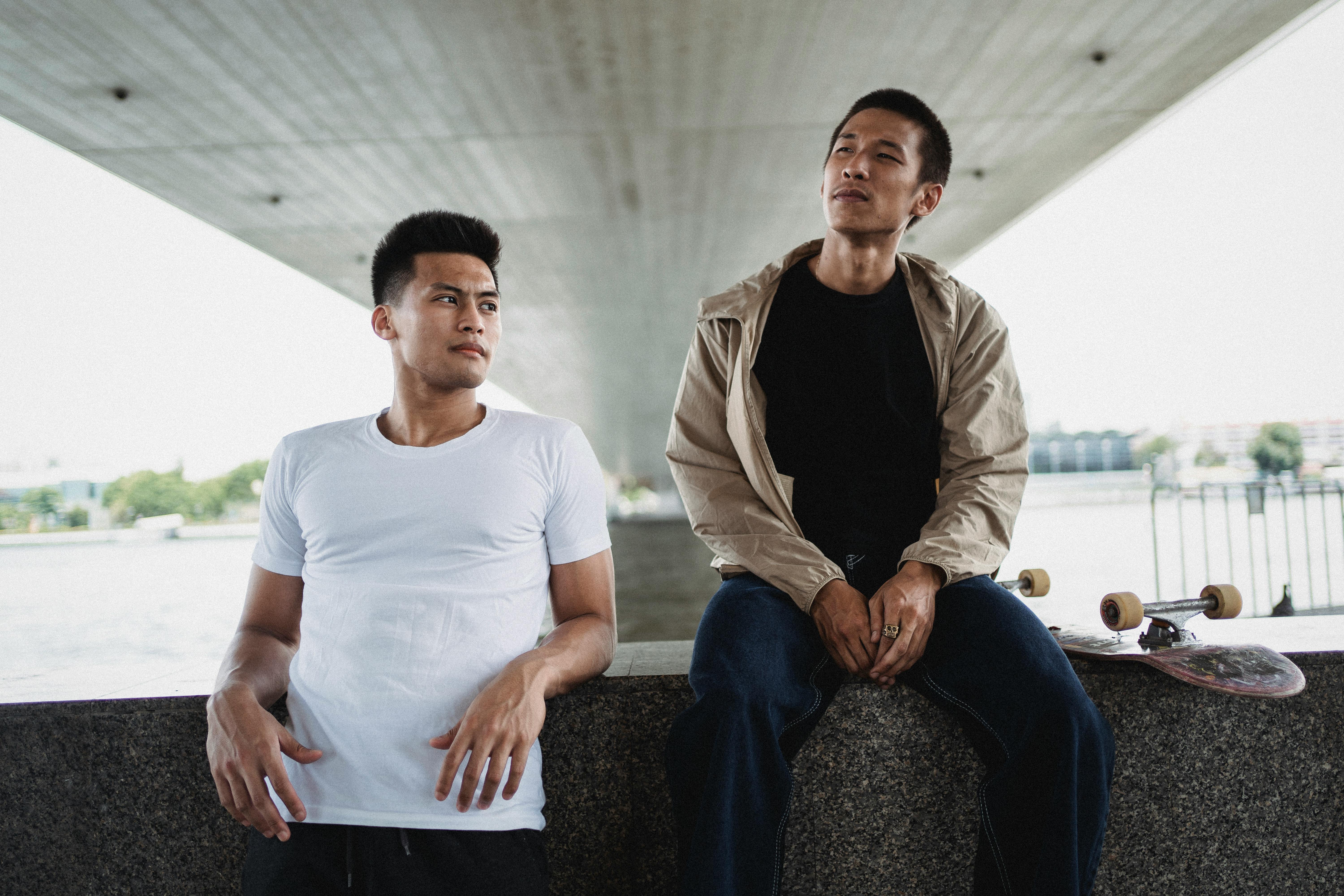 两个年轻人拿着滑板，坐在桥下，享受户外的轻松时刻