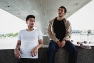 两个年轻人拿着滑板，坐在桥下，享受户外的轻松时刻