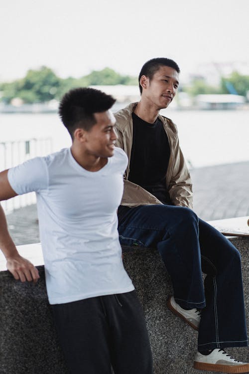 Positive multiracial friends in sportswear smiling and resting on building against square in daytime