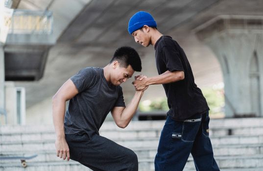 Side view of cool young guy in blue beanie  helping best friend in sportswear to stand up while training together in skate park