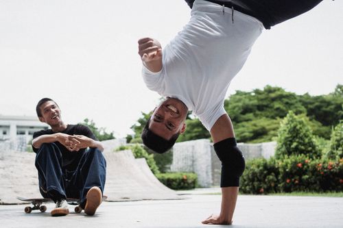 Free Happy guy standing in hand and looking at camera near admiring guy sitting on skateboard in skatepark in daytime Stock Photo