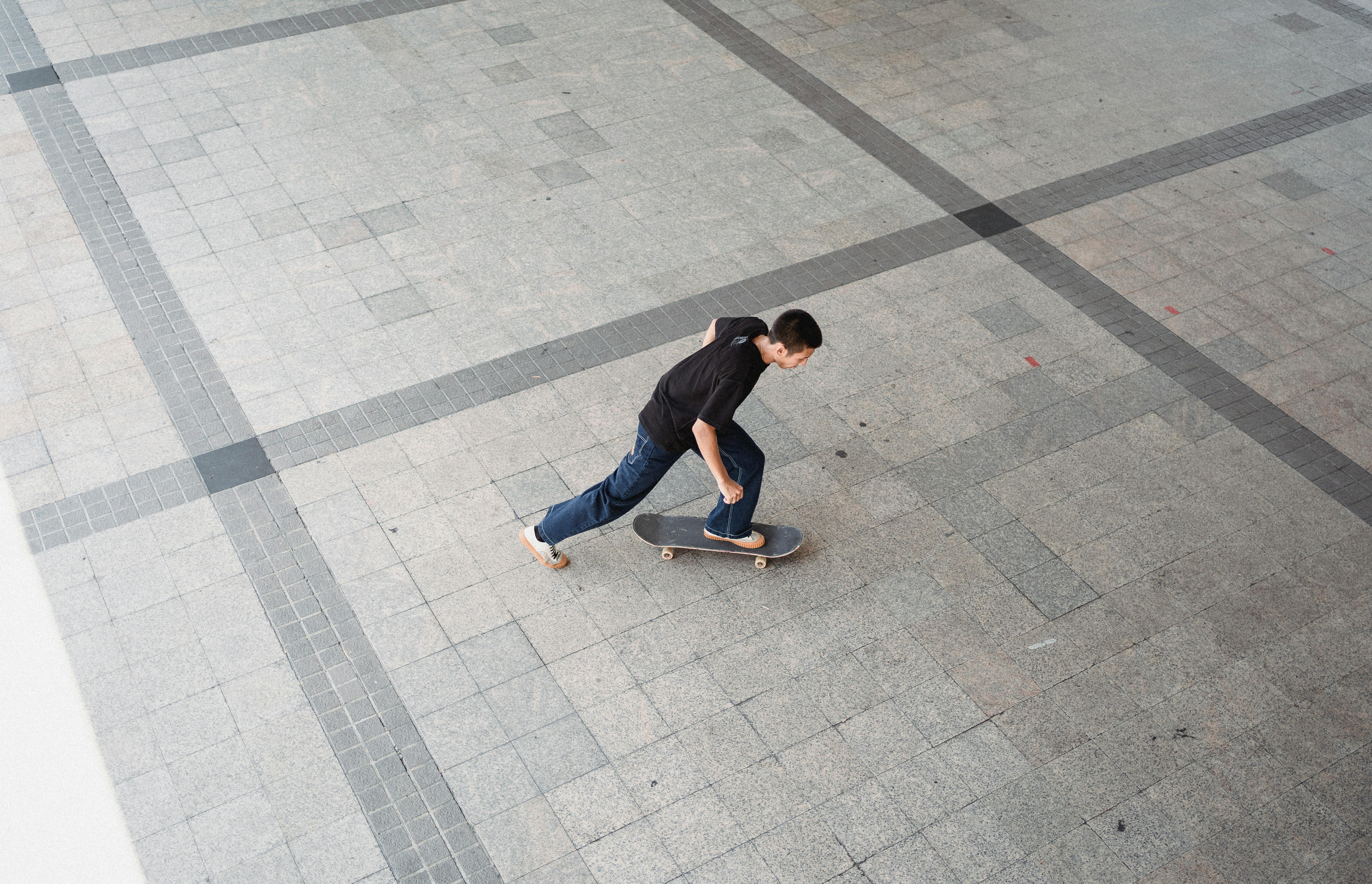 From above of faceless male skater in casual outfit riding skateboard on pavement