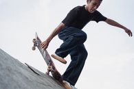 From below of crop young ethnic male athlete with skateboard practicing on platform under white sky while looking down