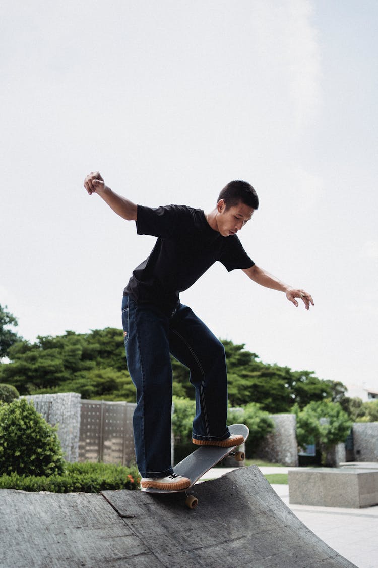 Asian Skateboarder Balancing On Skateboard On City Ramp