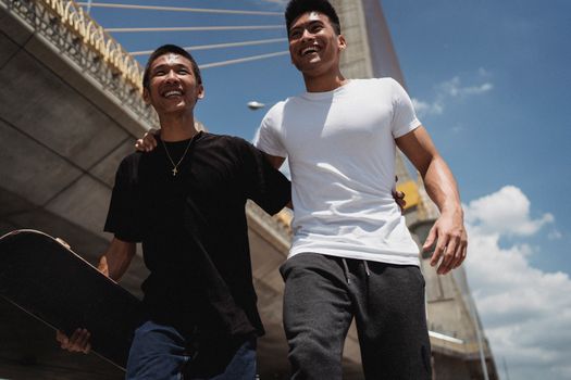 在城市桥梁附近，一位快乐的少数族裔男性运动员一边漫步，一边展望未来，并拥抱滑板