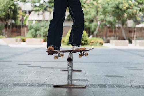 Crop unrecognizable sportsman practicing on skateboard rail above pavement in urban skate park in summer