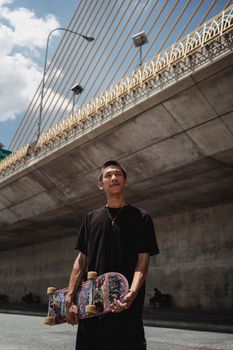 一位年轻的亚洲男运动员，在镇上多云的天空下，带着滑板沉思着向外望去