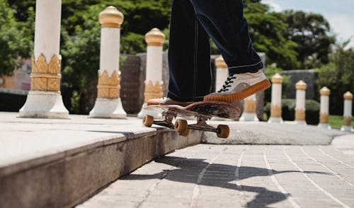 Crop unrecognizable male athlete on skateboard practicing on pavement with shade in town in sunlight