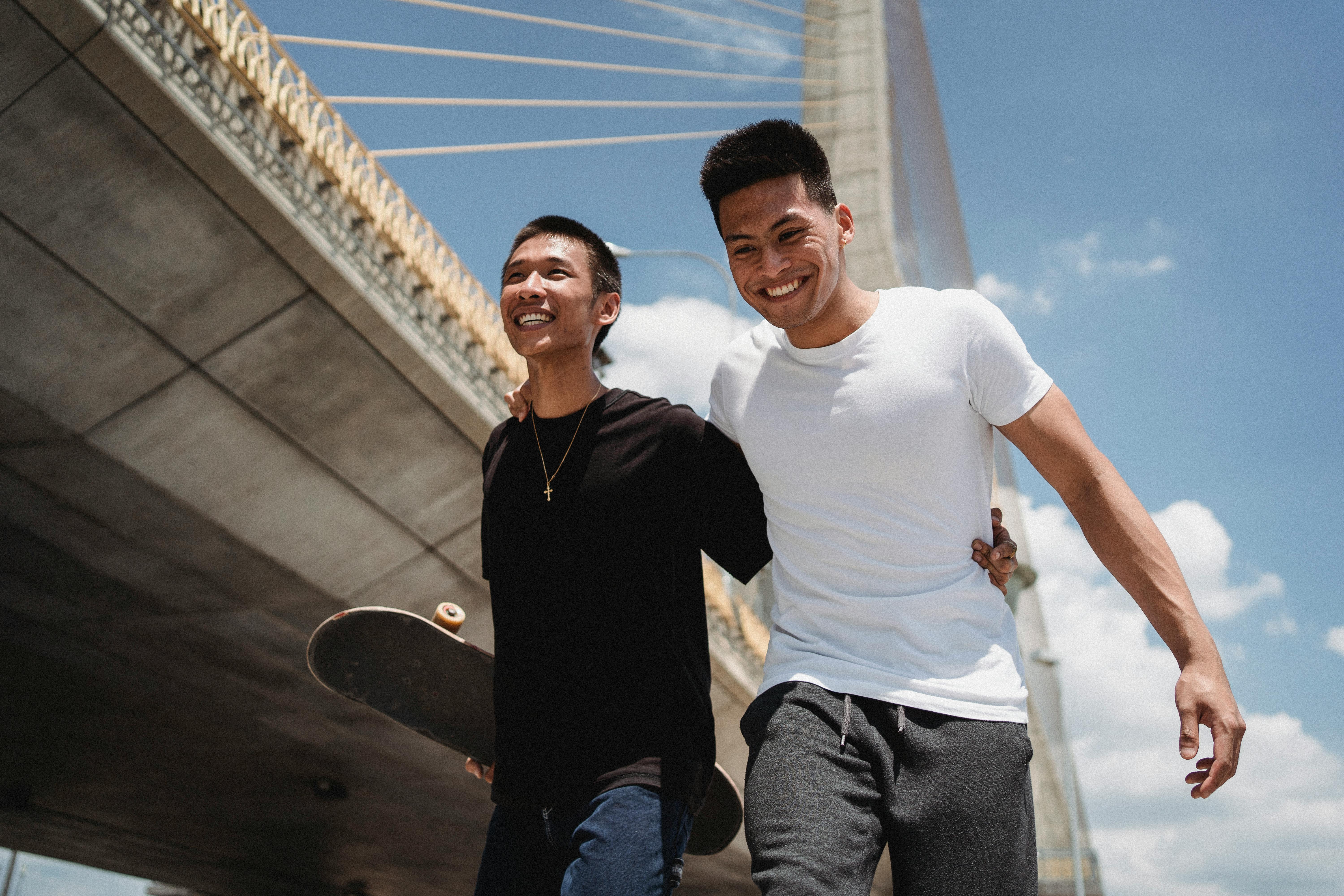 在一个阳光明媚的日子里，两个年轻人愉快地走在桥下，互相拥抱