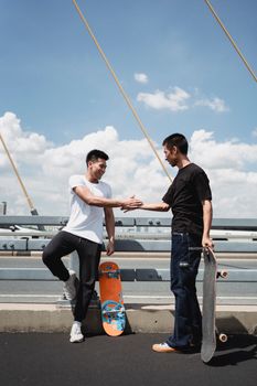 晴朗的天空下，两名男子在桥上用滑板互相致意，这是玩滑板的完美一天