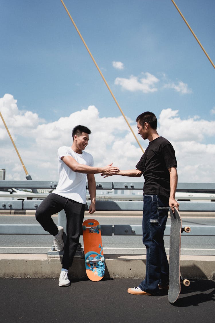 Asian Skateboarders Greeting Each Other On Suspension Bridge