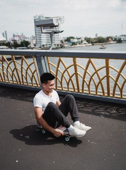 夏天，一名快乐的少数族裔年轻男运动员在栅栏桥的人行道上玩滑板，身影笼罩在阴影中