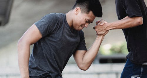 Crop anonymous male holding hand of young muscular ethnic partner with strained face on city street