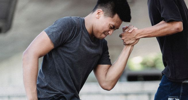 Crop anonymous male holding hand of young muscular ethnic partner with strained face on city street