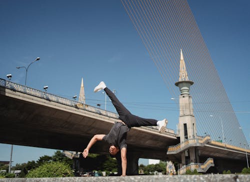 Full body of fit male in sportswear doing handstand while dancing break near urban bridge