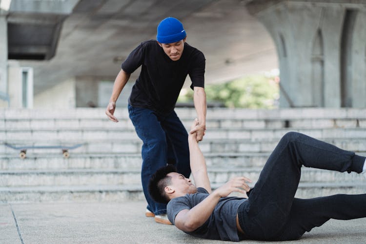 Young Asian Man Helping Friend On Pavement