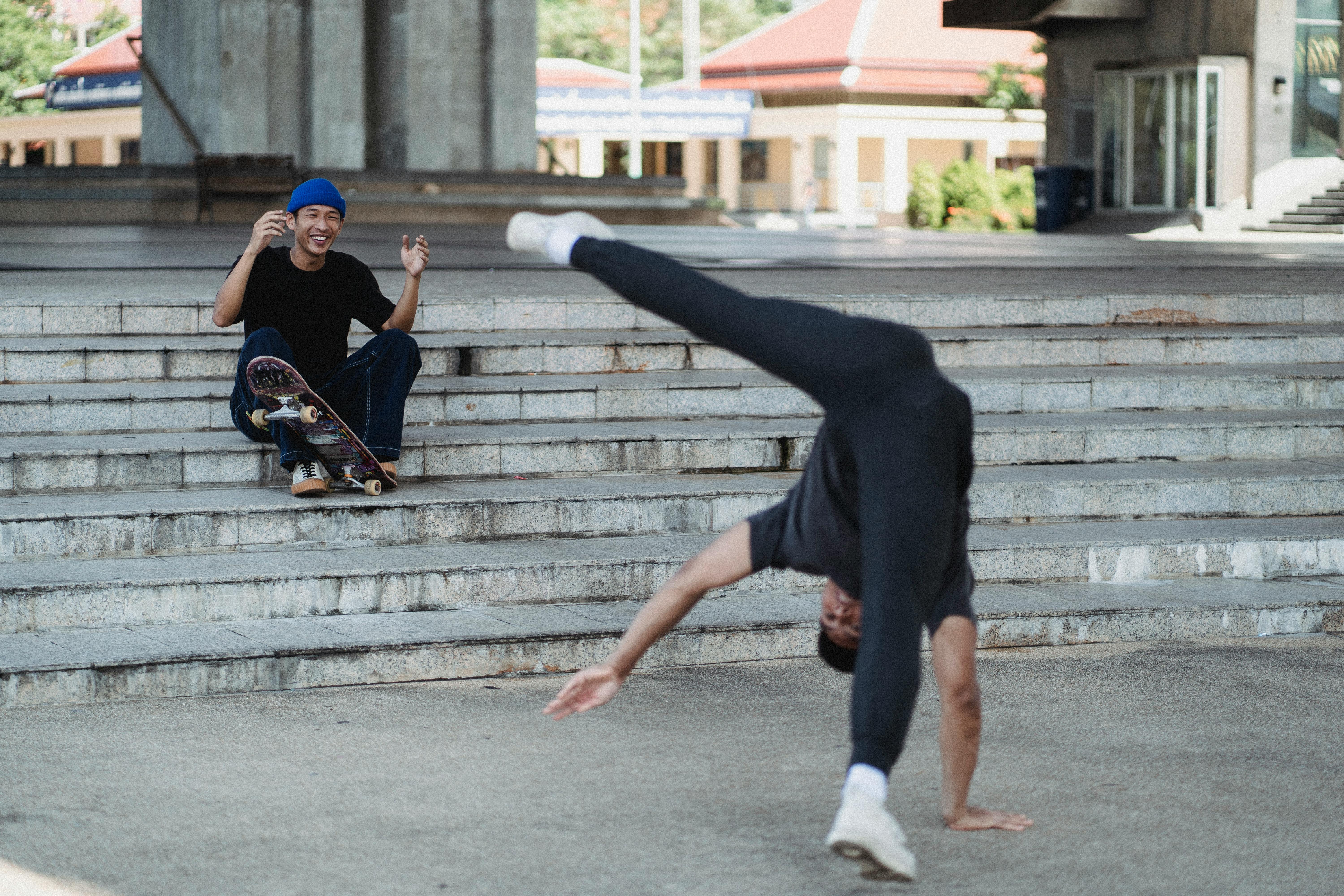 Two men showcase breakdancing and skateboarding in a vibrant urban setting.