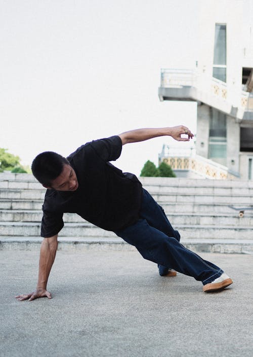 Full body of Asian male in casual clothes breakdancing on asphalt street near stairs