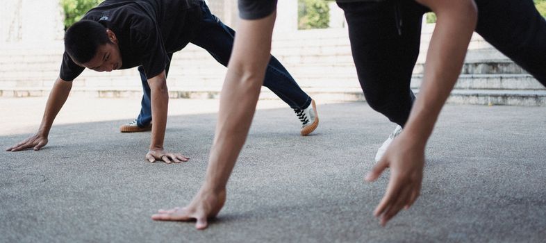 Young ethnic friends in casual clothes doing exercise while dancing break on asphalt city street