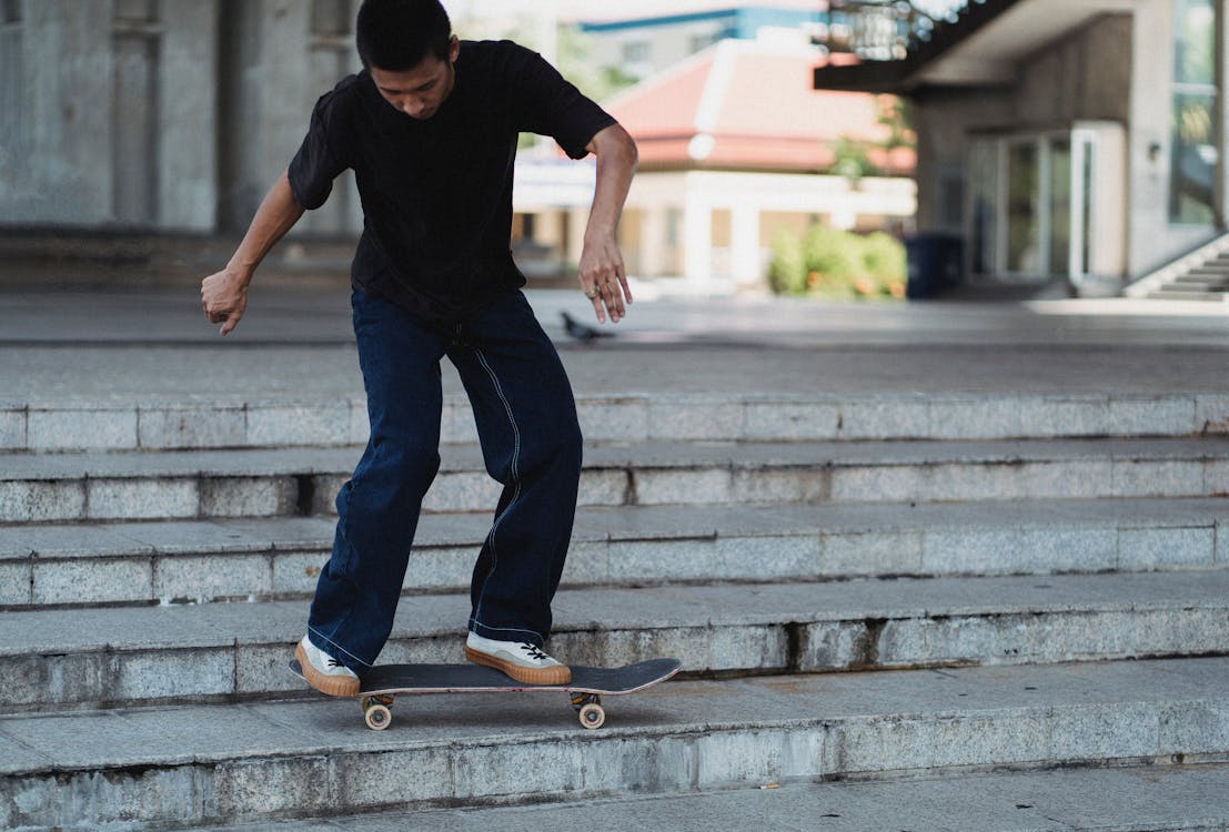 Full body of young male in casual outfit performing trick on skateboard while spending time on urban staircase